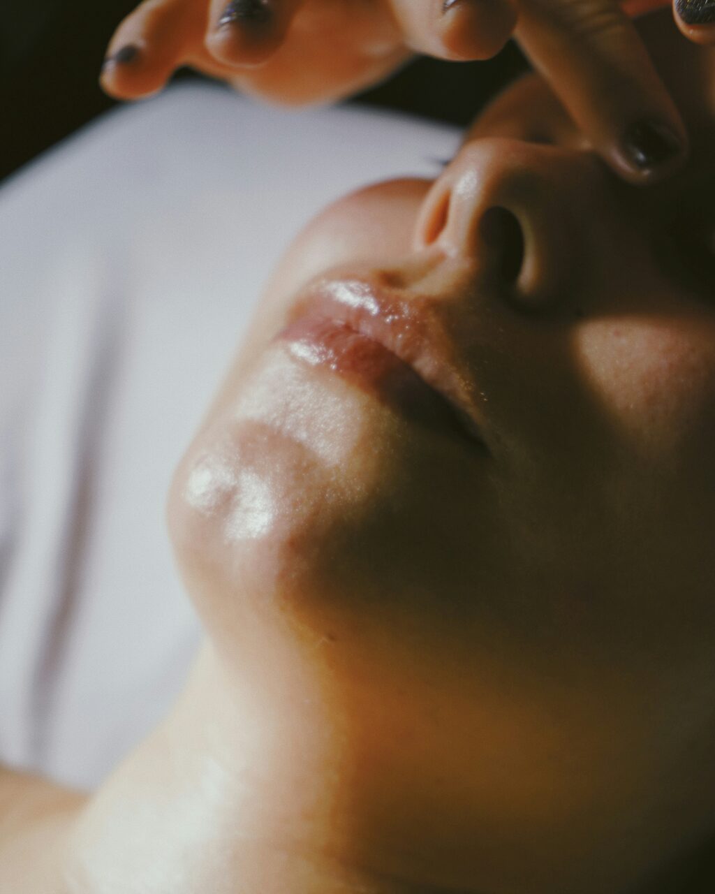 A woman lying back with her eyes closed during a facial treatment in warm, soft daylight